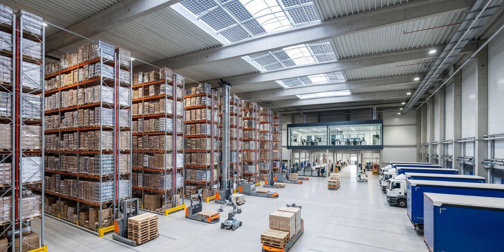 Interior view of a modern logistics property: High shelves full of goods (just-in-case), automated warehouse robots and driverless transport systems in use. Energy-efficient hall with PV system.